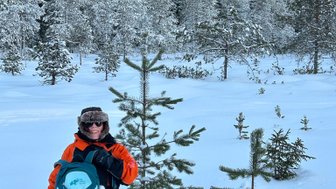Eine Person mit einem Rucksack steht im tiefen Schnee, umgeben von schneebedeckten Bäumen und einer klaren blauen Himmel.