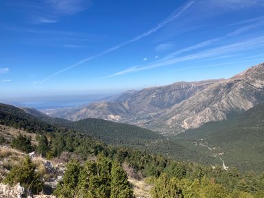 Ein atemberaubender Blick auf die Berge und das grüne Tal, das sich bis zum blauen Meer erstreckt, unter einem klaren Himmel.