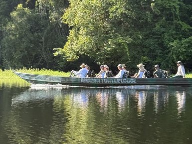 Eine Gruppe von Menschen sitzt in einem Boot und genießt die Zeit auf einem ruhigen Gewässer umgeben von dichtem Grün.