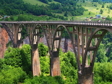 Eine beeindruckende Brücke mit eleganten Bögen, die über eine grüne Schlucht führt, umgeben von üppiger Vegetation.