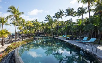 Ein luxuriöser Pool umgeben von Palmen und Liegen, ideal für Entspannung unter dem klaren Himmel von Mauritius.