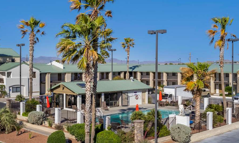 Ein sonniger Außenbereich eines Hotels mit einem Pool, umgeben von Palmen und gepflegten Pflanzen.