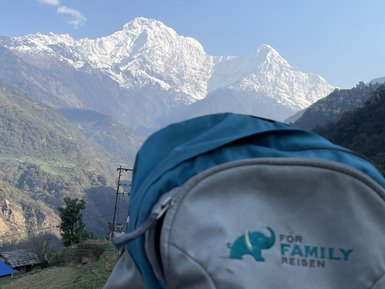 Ein blauer Rucksack mit einem Elefantenlogo steht im Vordergrund, während majestätische schneebedeckte Berge im Hintergrund leuchten.