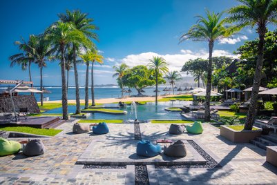 Ein luxuriöser Poolbereich mit Palmen und Liegen, umgeben von einem atemberaubenden Blick auf das Meer und den Strand.
