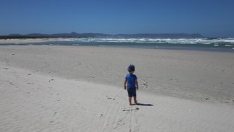 Kleines Kind spielt am Sandstrand von Hermanus mit Blick auf das Meer – Garden Route mit Kindern