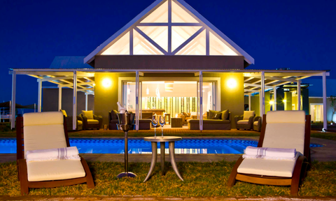 Eine Safari Lodge bei Nacht mit Pool im Vordergrund, Liegestühlen und beleuchtetem Gebäude im Hintergrund - Namibia Familienreise