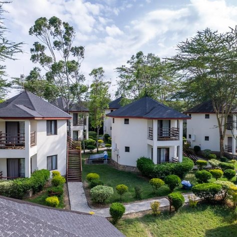 Die Ansicht zeigt mehrere moderne Lodges mit dunklen Dächern, umgeben von üppigem Grün und gepflegten Gärten.