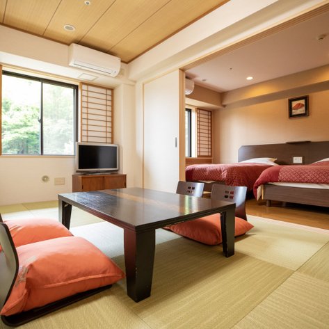 Ein traditionelles japanisches Zimmer mit einem niedrigen Tisch, zwei roten Futons und einem Fenster, das auf einen grünen Garten blickt.