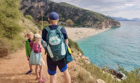 Eine Familie wandert auf einem Pfad mit Blick auf einen schönen Strand und das klare, blaue Wasser des Meeres.