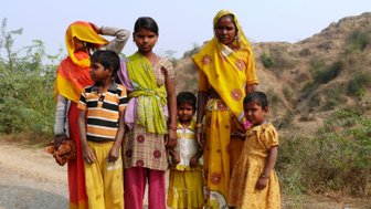 Eine Gruppe von fünf Personen steht an einem Weg, umgeben von sanften Hügeln und grüner Vegetation.