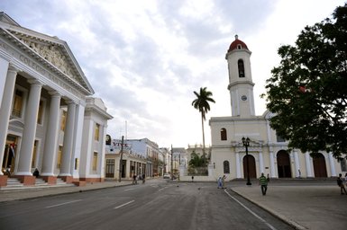 Eine ruhige Straße in Cienfuegos, gesäumt von historischen Gebäuden und einer Kirche mit einem markanten Glockenturm.
