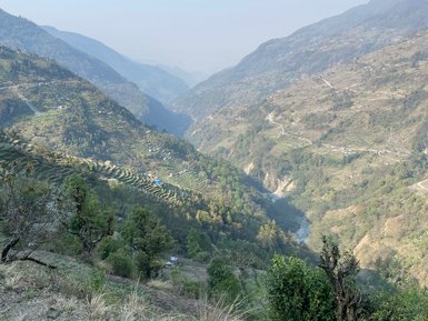 Eine atemberaubende Berglandschaft in Nepal mit sanften Hügeln und terrassierten Feldern, die in der Ferne verschwommen sind.