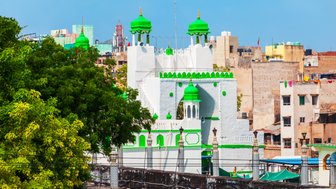 Eine prächtige weiße Struktur mit grünen Kuppeln und Verzierungen, umgeben von städtischen Gebäuden und Bäumen.