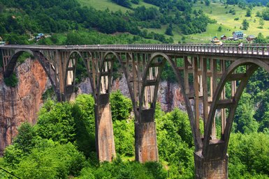Eine beeindruckende Brücke mit eleganten Bögen, die über eine grüne Schlucht führt, umgeben von üppiger Vegetation.