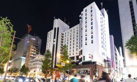 Ein modernes Hotelgebäude mit beleuchteten Fenstern, umgeben von urbaner Architektur und nächtlicher Atmosphäre.