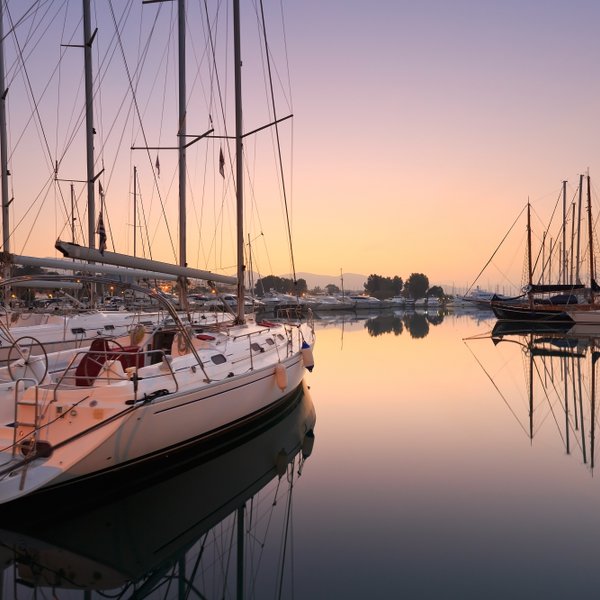 Eine ruhige Marina bei Sonnenaufgang, mit mehreren Segelbooten, die sanft im Wasser schaukeln und ihre Spiegelungen zeigen.