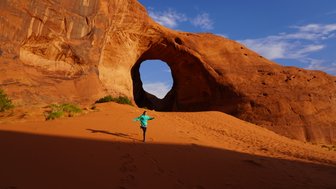 Ein Kind in einem blauen Pullover läuft fröhlich durch die rote Sandlandschaft von Monument Valley, umgeben von beeindruckenden Felsen.