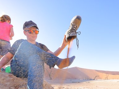 Ein Kind leert seinen Schuh aus, in dem sich Sand befindet - Namibia Rundreise mit Kindern