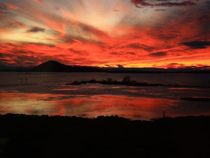 Ein atemberaubender Sonnenuntergang über einem ruhigen Gewässer, mit leuchtend roten und orangefarbenen Wolken am Himmel.