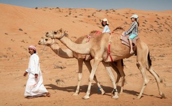 Beduine führt zwei Kamele mit zwei Mädchen durch die Wüste – Oman Familienreise