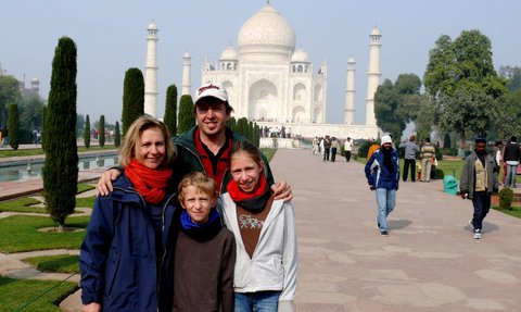 Eine Familie posiert fröhlich vor dem Taj Mahal, umgeben von grünen Bäumen und einem klaren Himmel.