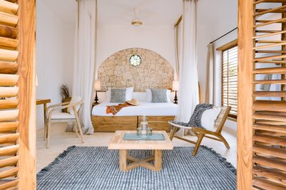 Ein stilvolles Schlafzimmer mit einem großen Bett, umgeben von sanften Vorhängen und einer Steinwand im Hintergrund.