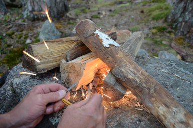Hände, die mit einem Feuerstein Funken erzeugen, während sie Holzscheite für ein Lagerfeuer vorbereiten.