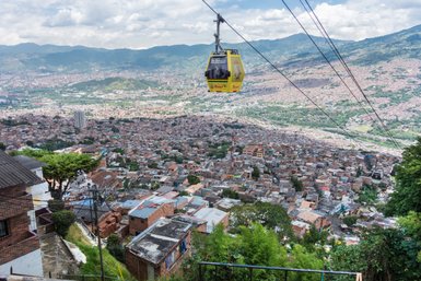 Eine Seilbahn schwebt über die dicht besiedelten Hügel von Medellín, umgeben von grünen Bergen und einer weiten Stadtansicht.