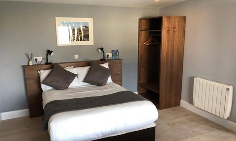 Ein modernes Hotelzimmer mit einem großen Bett, dekoriert mit braunen Kissen und einem stilvollen Holzschrank.