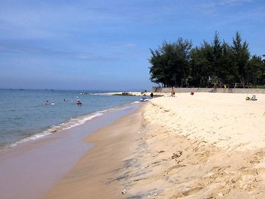 Ein sonniger Strand mit feinem Sand, wo Menschen im Wasser schwimmen und am Ufer entspannen.