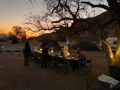 Eine Reisegruppe sitzt am Abend an einem Tisch bei Sonnenuntergang - Namibia mit Jugendlichen