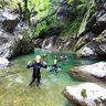 Eine Gruppe von Menschen in Neoprenanzügen genießt das Wasser eines klaren Flusses, umgeben von hohen Felsen und Bäumen.