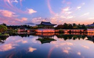 Ein malerischer Sonnenuntergang über dem Donggung Wolji Teich, mit reflektierenden Wolken und historischen Gebäuden im Hintergrund.