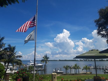 Eine amerikanische Flagge weht über einem malerischen Hafen mit Booten und üppigen Palmen im Vordergrund.