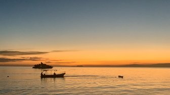 Ein ruhiger Sonnenuntergang über dem Meer, mit sanften Wellen und einem Boot, das langsam in der Ferne fährt.