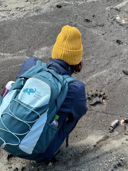 Eine Person mit einer gelben Mütze untersucht den Boden, während sie auf einem sandigen Untergrund sitzt.