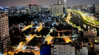 Ein nächtlicher Blick auf die beleuchteten Straßen von Saigon, mit Hochhäusern und einem ruhigen Fluss im Hintergrund.