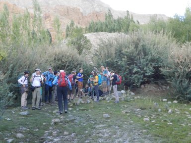 Eine Gruppe von Wanderern macht eine Pause in der Natur, umgeben von Büschen und Bergen im Hintergrund.