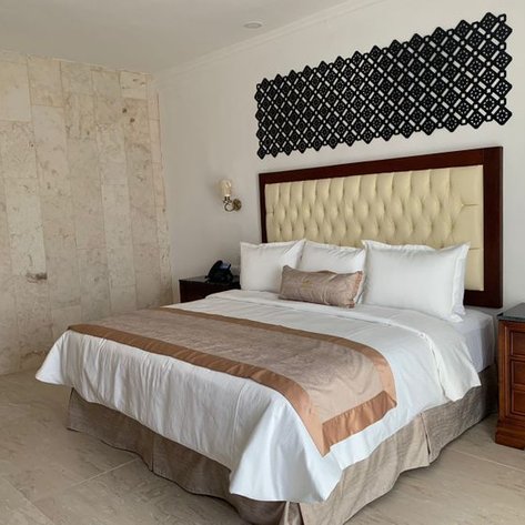 Ein elegantes Schlafzimmer mit einem großen Bett, das mit weißen und beigen Kissen dekoriert ist, und einer stilvollen Wandverkleidung.