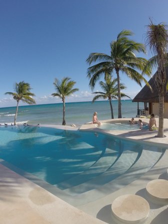 Ein einladender Poolbereich mit Palmen, wo Familienmitglieder entspannt im Wasser spielen und die Sonne genießen.