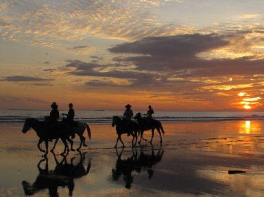 Reitergruppen genießen gemächlich den Sonnenuntergang am Strand, während sich der Himmel in warmen Farben färbt.