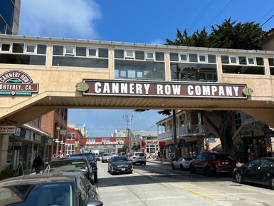 Die Cannery Row Company in Monterey, Kalifornien, ist von Geschäften und Autos umgeben, unter einem blauen Himmel.