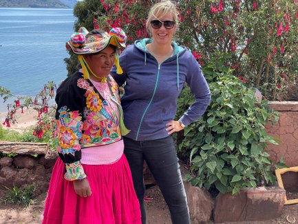 Eine einheimische Frau in traditioneller Kleidung steht neben einer Frau mit Sonnenbrille, beide lächeln vor einer malerischen Kulisse.