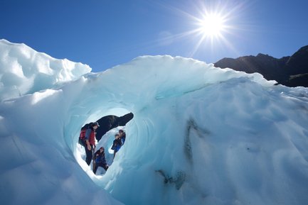 Eine Gruppe von Wanderern erkundet eine beeindruckende Eishöhle unter strahlend blauem Himmel und hellem Sonnenlicht.