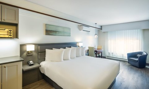 Ein modernes Hotelzimmer mit einem großen Kingsize-Bett, das mit mehreren Kissen dekoriert ist.