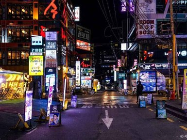 Eine belebte Straße in Gangnam, beleuchtet von bunten Neonlichtern und Werbetafeln, die das nächtliche Stadtleben zeigen.