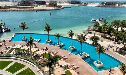 Ein luxuriöser Poolbereich mit Palmen und Liegen, umgeben von klarem Wasser und einem schönen Ausblick auf die Küste.
