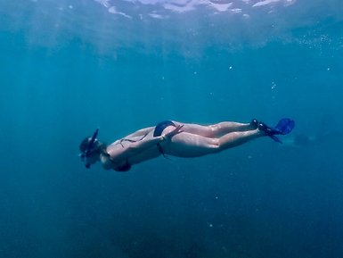 Eine Person taucht elegant unter Wasser und erkundet die ruhigen, blauen Tiefen des Ozeans mit einer Schnorchelausrüstung.