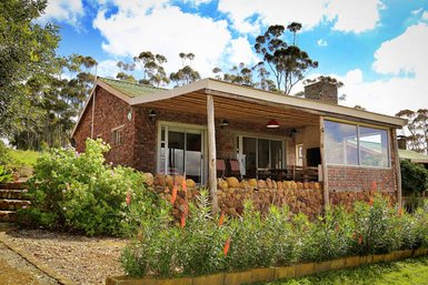 Ein charmantes, gemauertes Ferienhaus mit einem einladenden Garten und einer Veranda, umgeben von üppiger Natur.