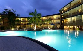 Ein beleuchteter Pool umgeben von Palmen und einem Hotel, das in der Dämmerung eine entspannende Atmosphäre schafft.